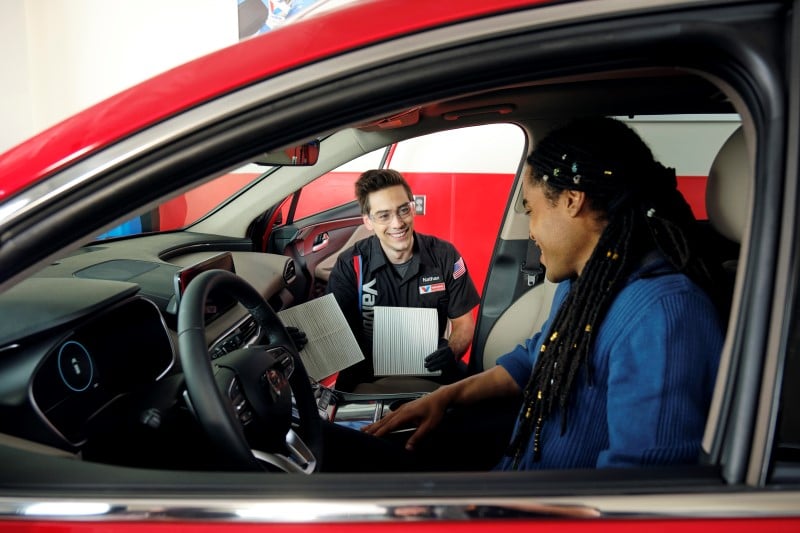 Valvoline Instant Oil Change technician offering a customer in a red car an air filter replacement