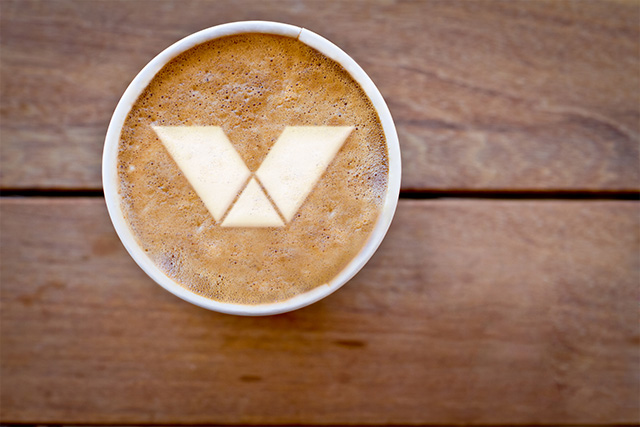 Valvoline logo in foam on top of coffee in paper cup on wooden surface,