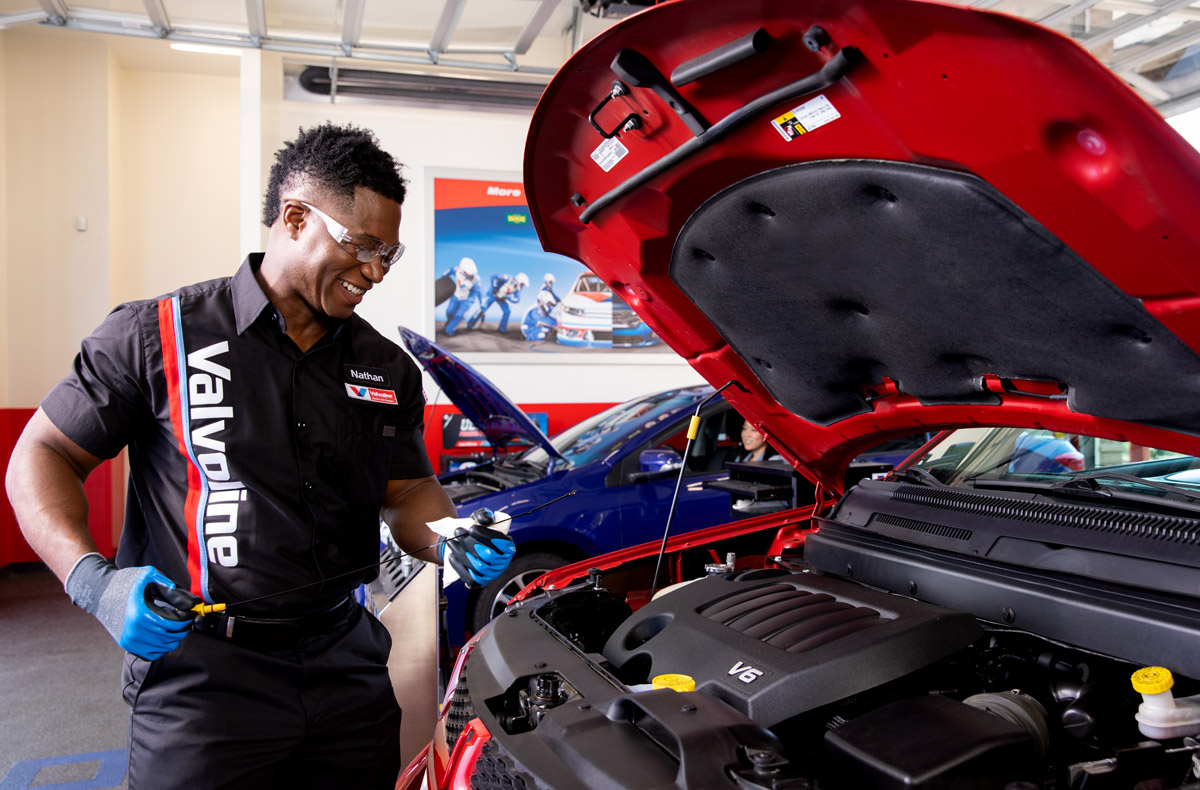 Valvoline technician performing an oil change under the hood of a red car