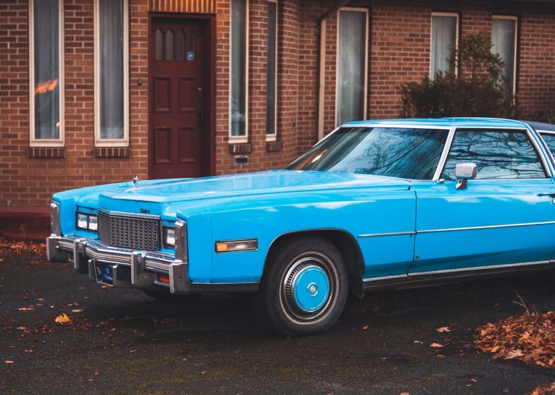 Light blue car on the street outside of a red brick house